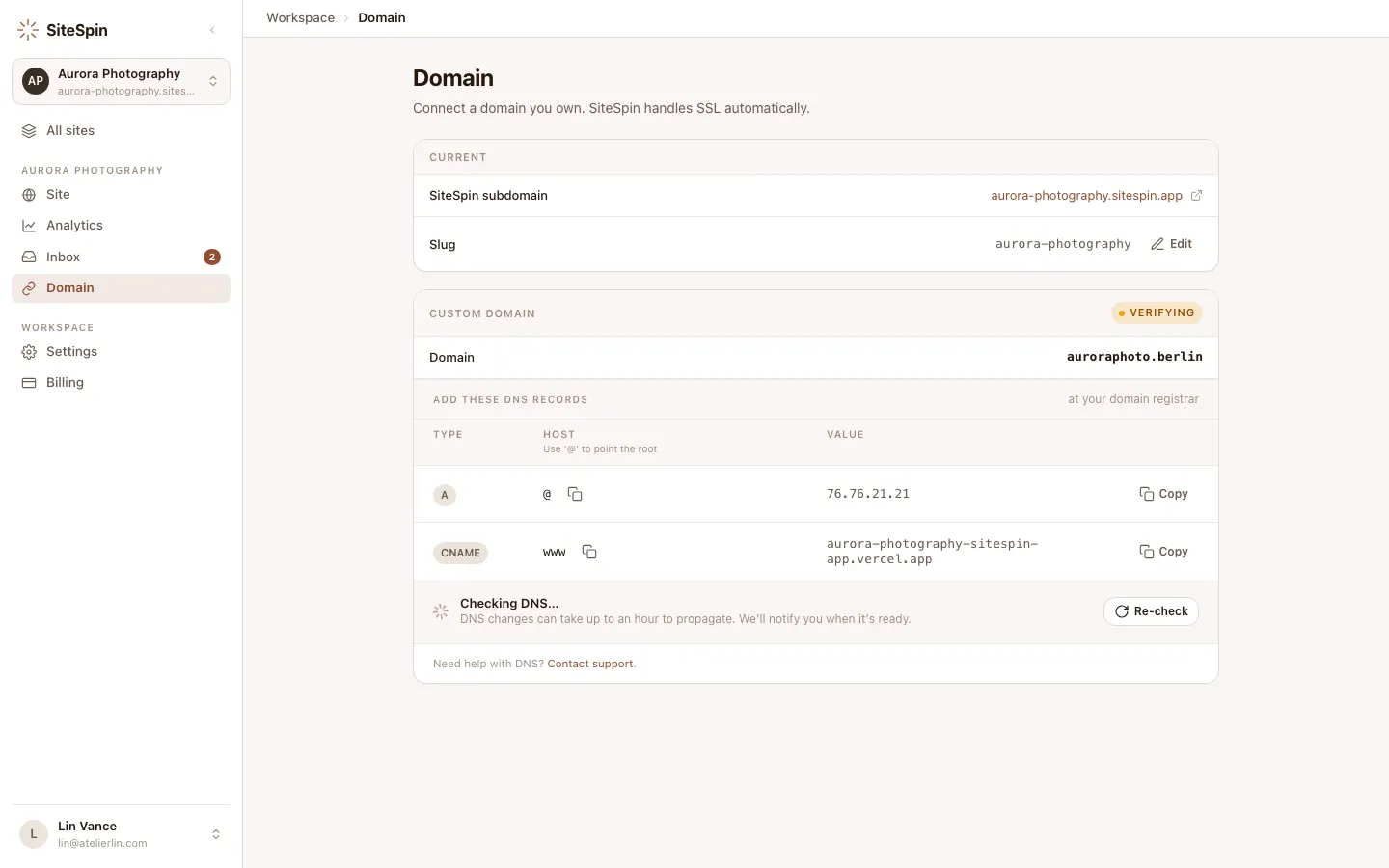 SiteSpin web app domain settings showing the DNS records helper for a custom domain. A and CNAME rows with copy buttons, a verifying status pill, and a 'Re-check' affordance.